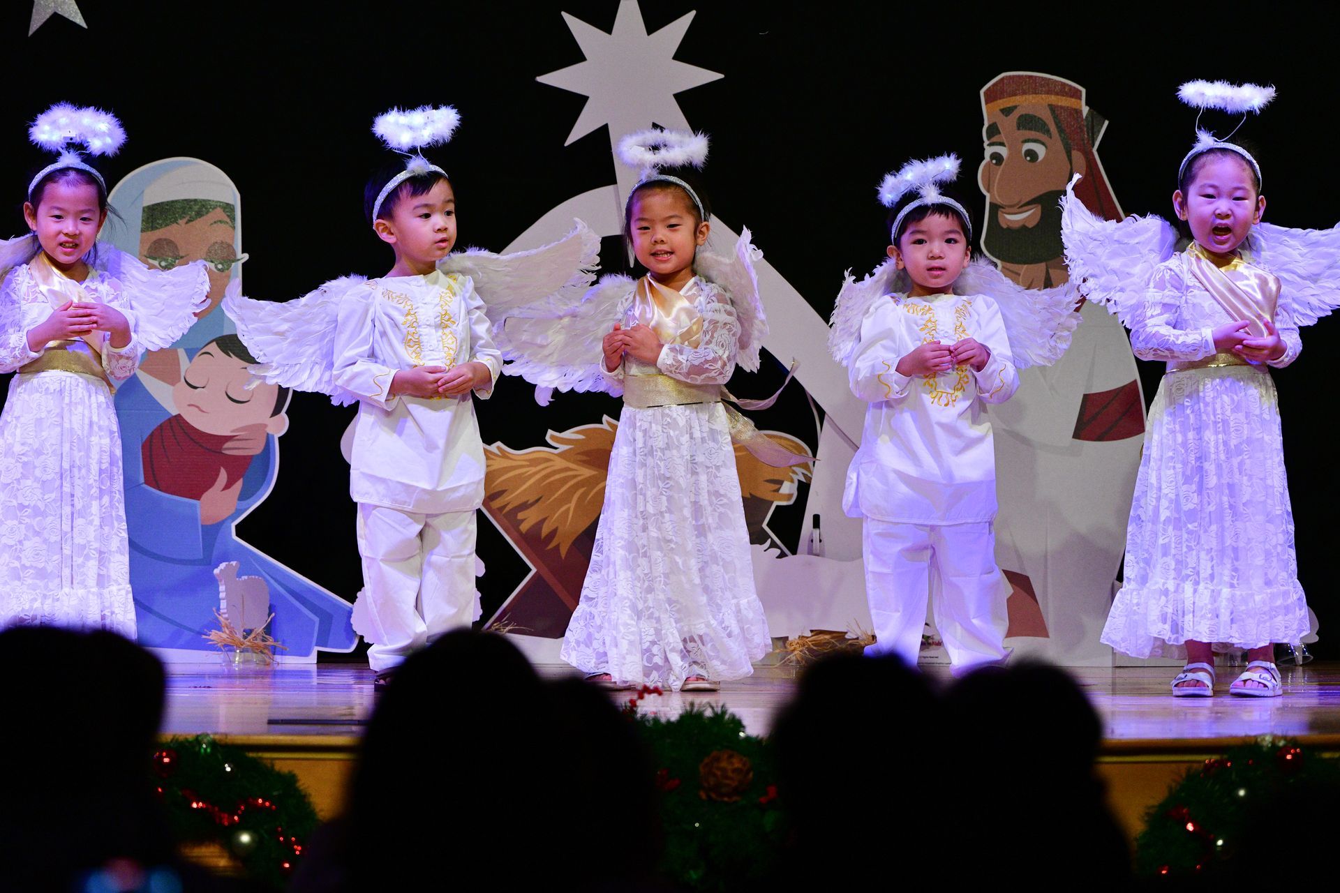 Children in angel costumes performing a Nativity scene on stage.