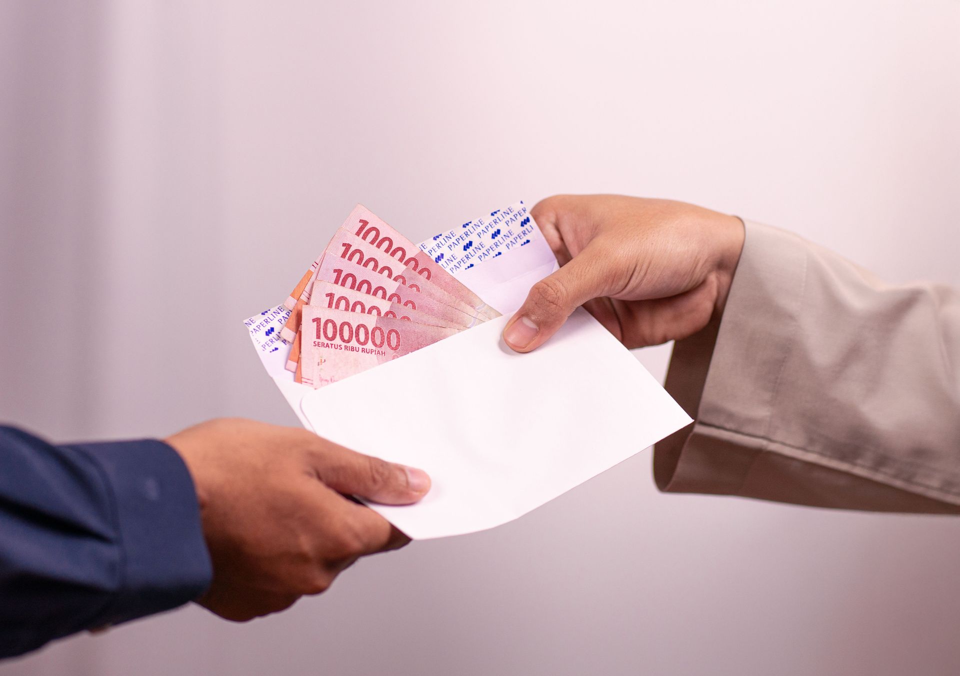 Two people exchange an open envelope with banknotes visible inside.