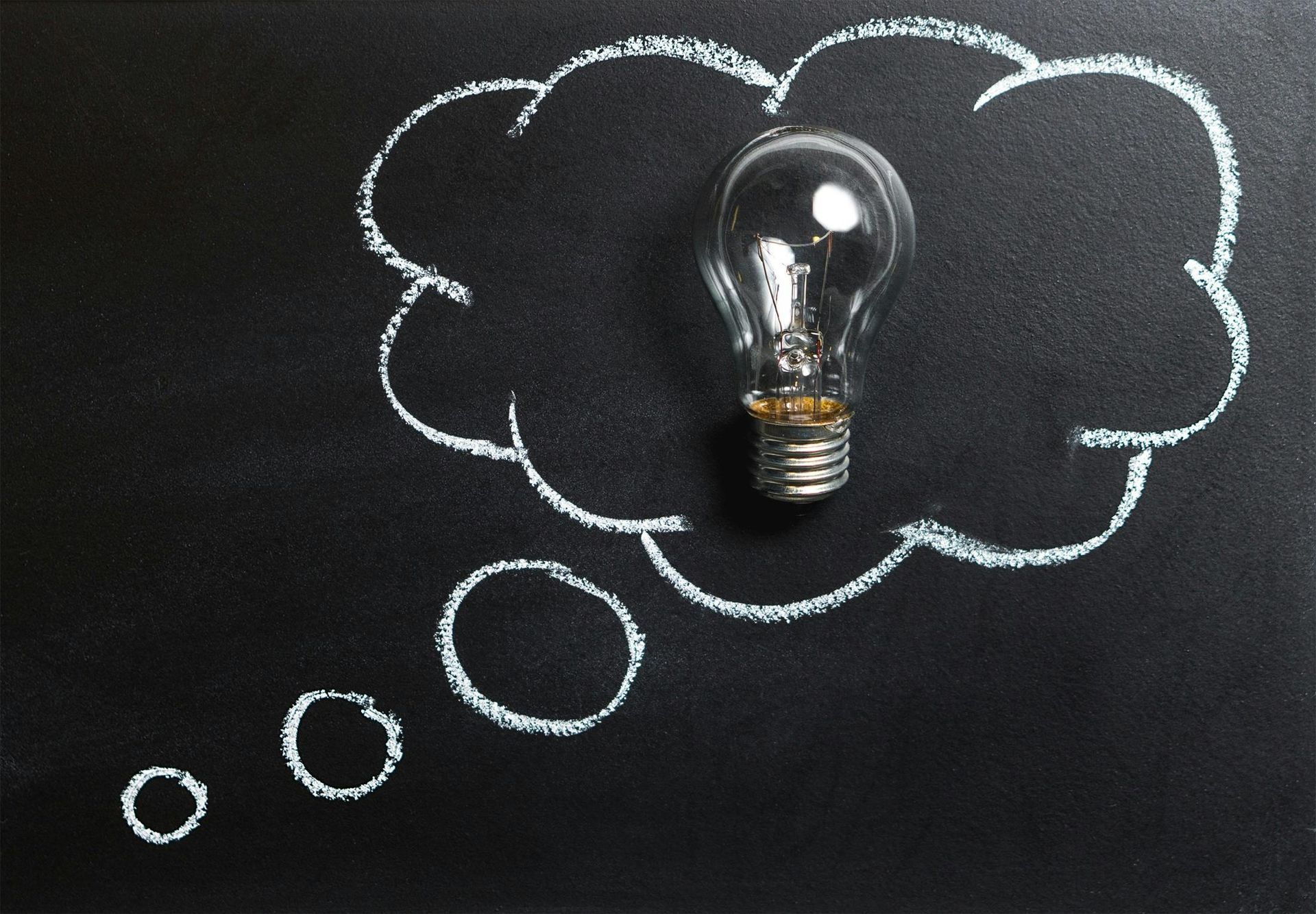 Lightbulb inside a white chalk thought bubble on a black chalkboard.
