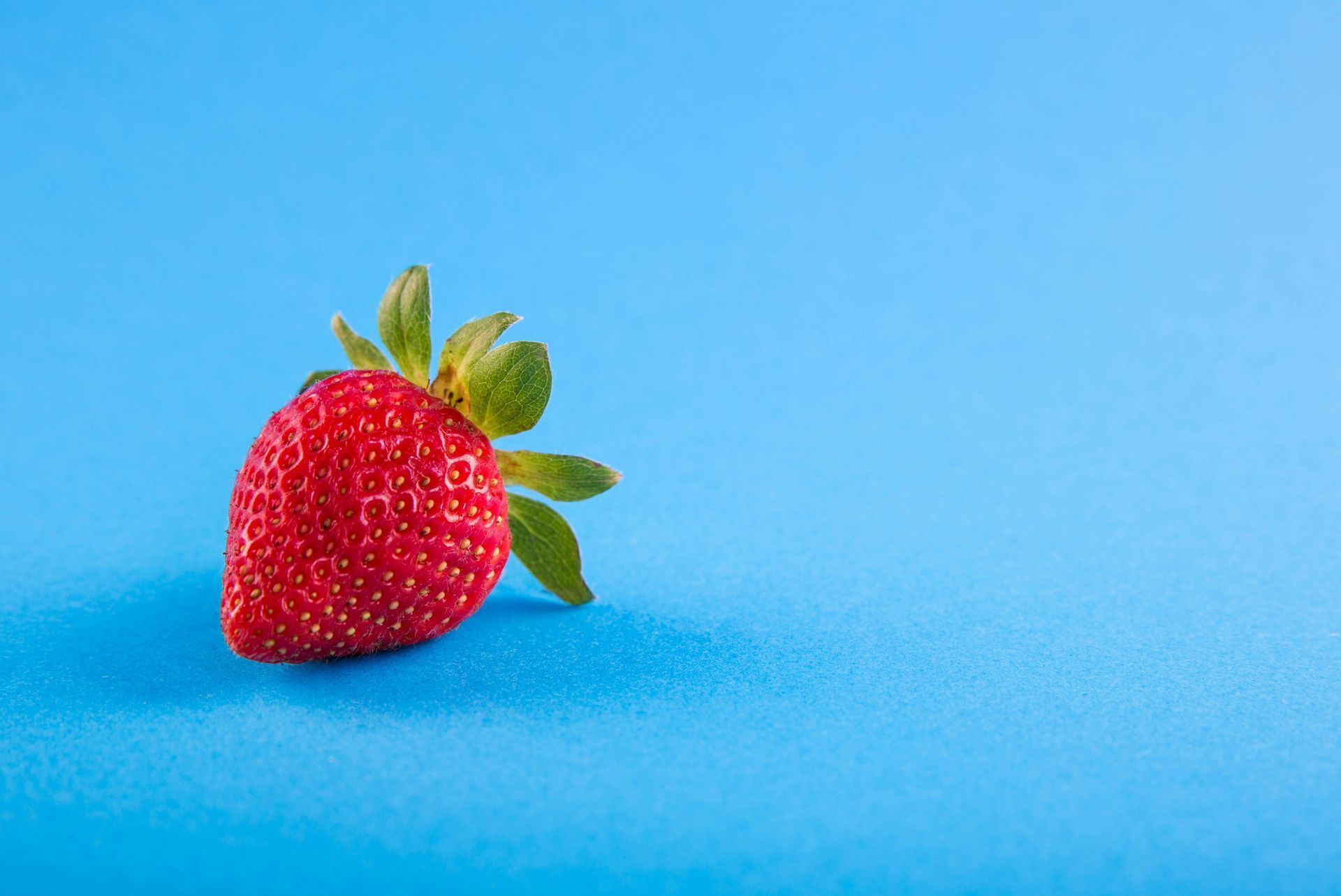 Red strawberry with green leaves on a bright blue background.
