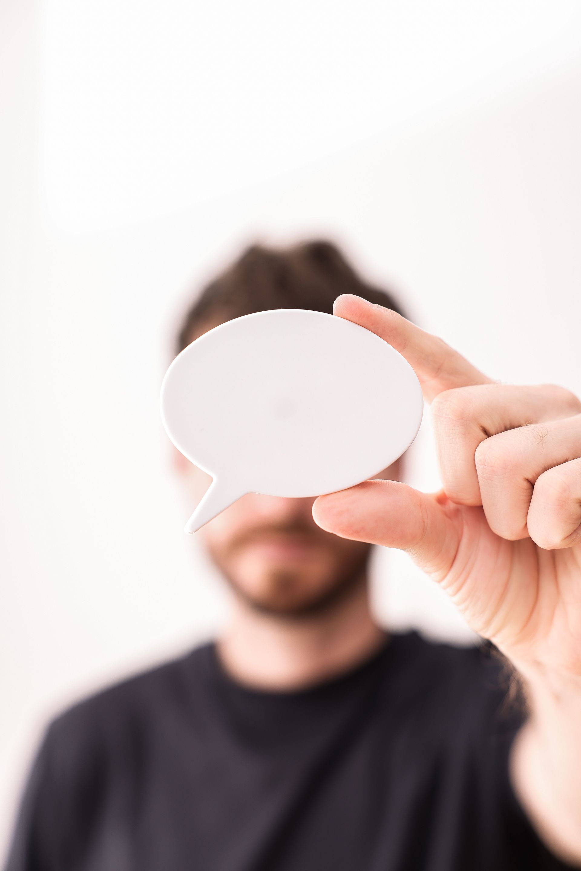Person holding a blank speech bubble card toward the camera against a white background