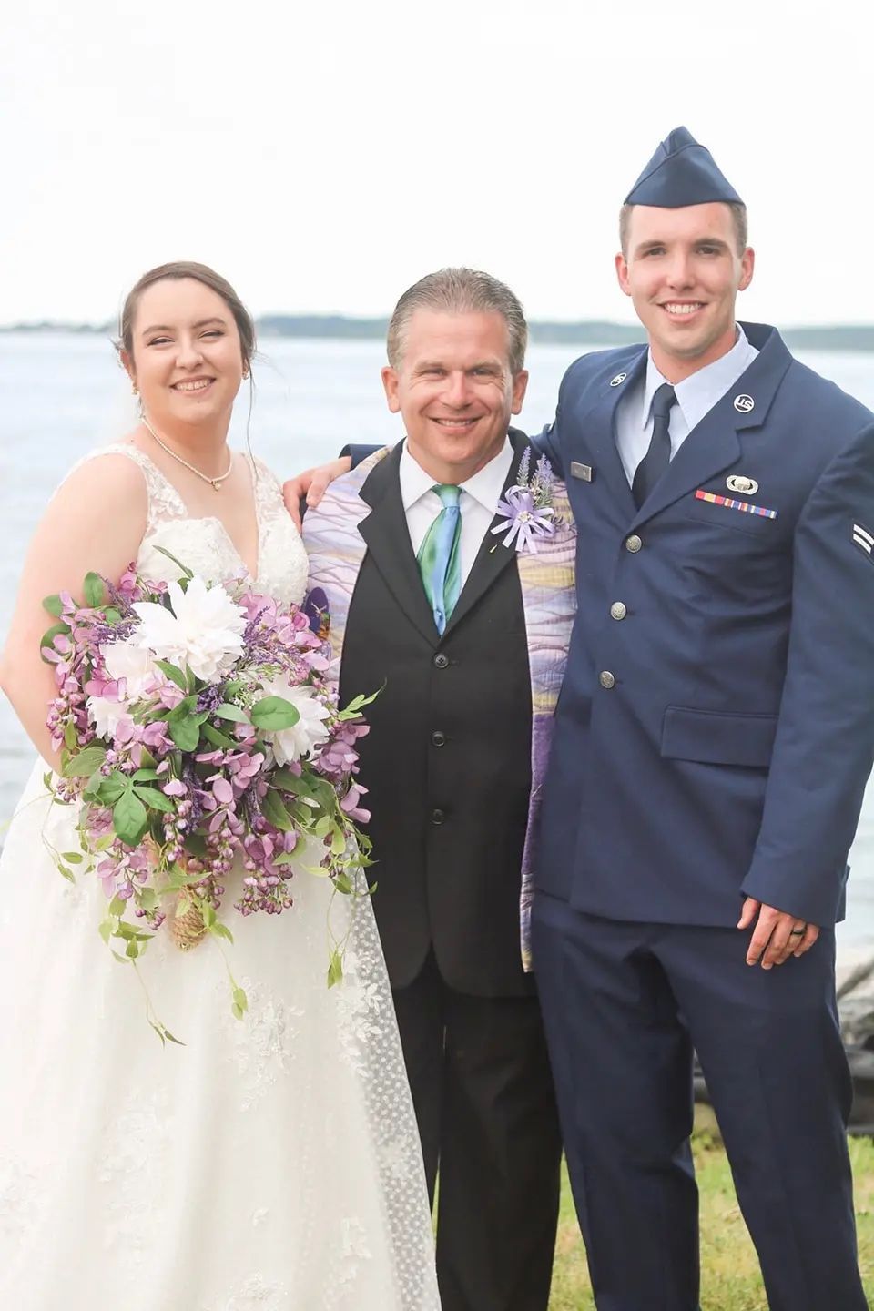 A bride and groom are posing for a picture with a man in a military uniform.