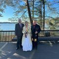 A bride and groom are posing for a picture on a deck overlooking a lake.