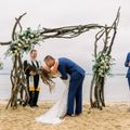 A bride and groom kissing under a wooden arch on the beach
