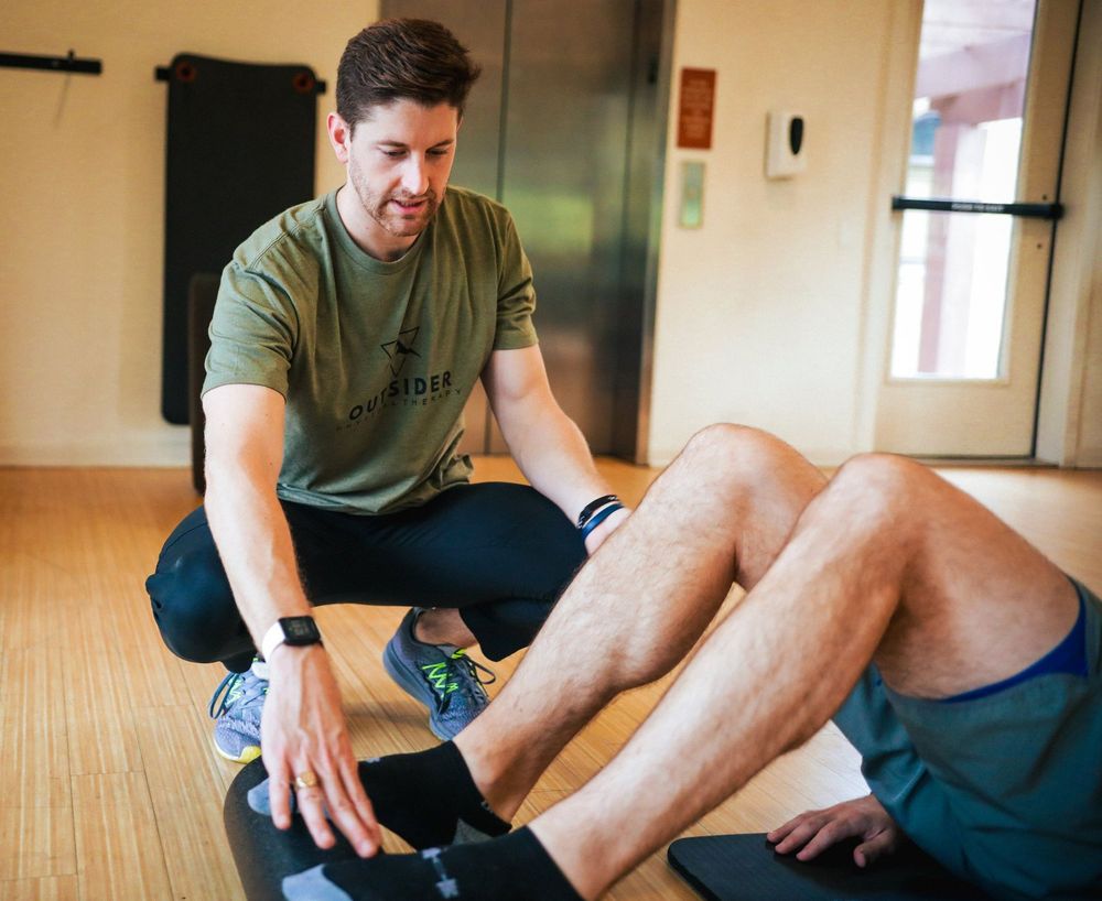 A man in a green shirt is stretching another man 's leg