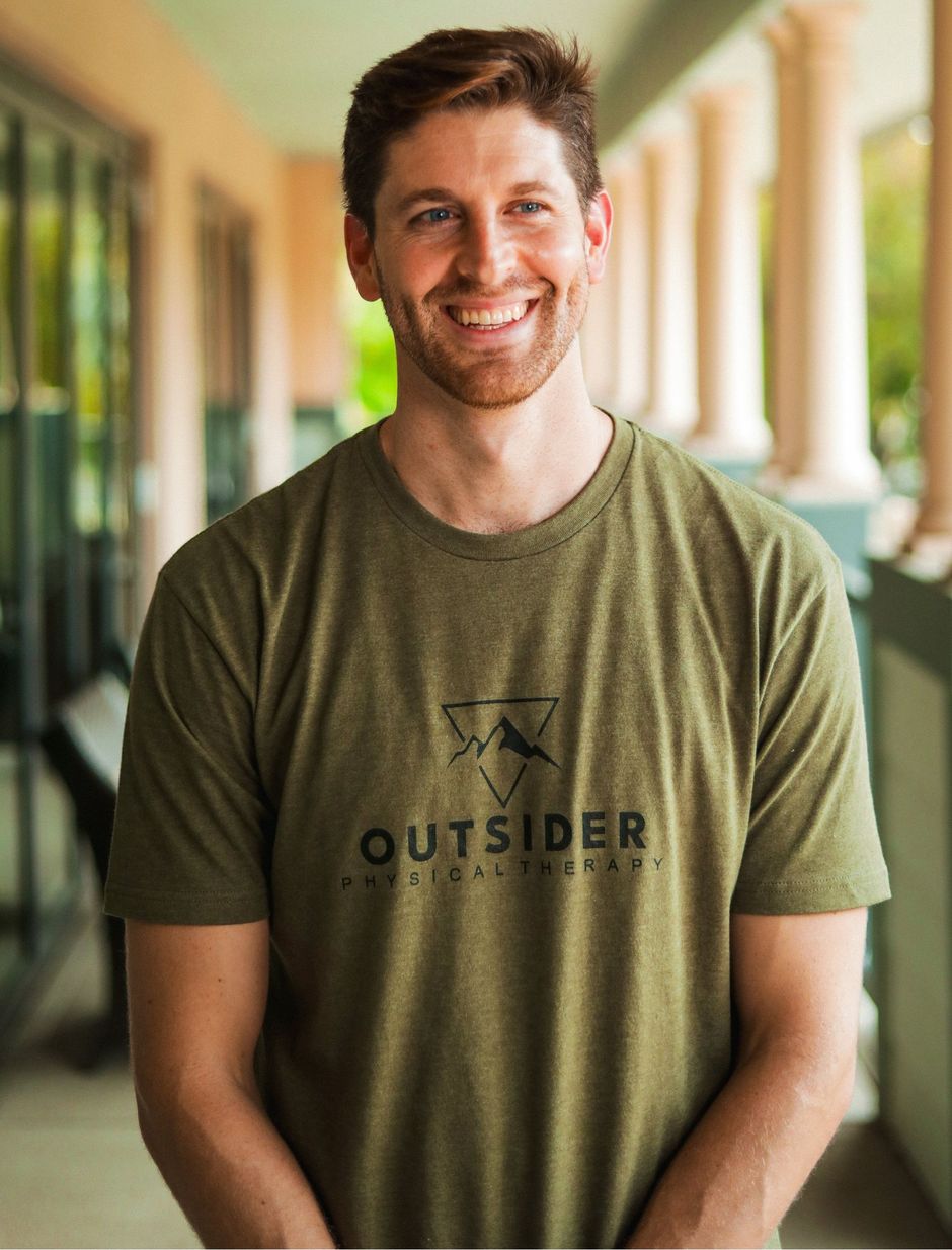 A man wearing a green t-shirt with the word outsider on it is smiling.
