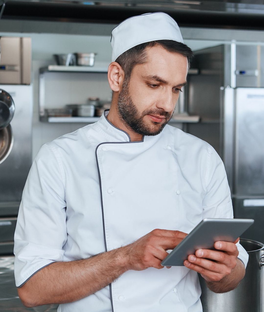 Chef in white uniform, using tablet in a commercial kitchen.