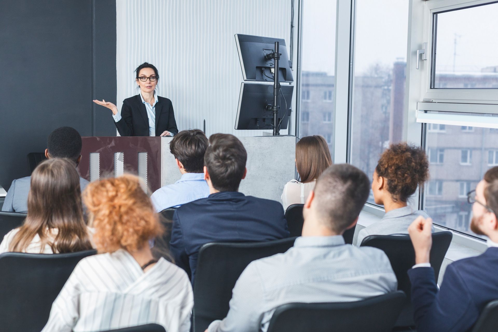 Woman speaking at a podium to a group seated in a conference room.