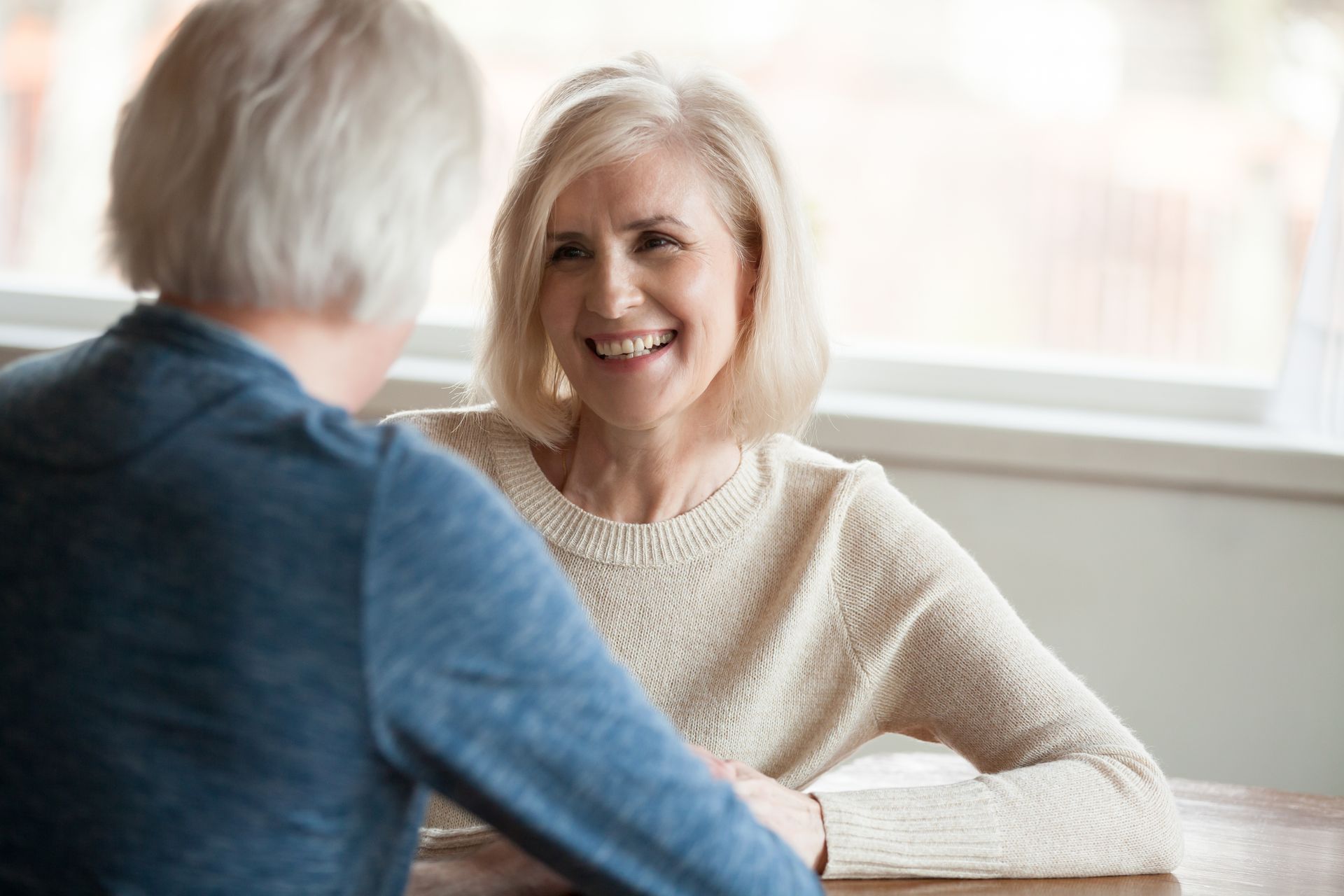Woman with blonde hair smiles while talking, seated across from another person at a table.