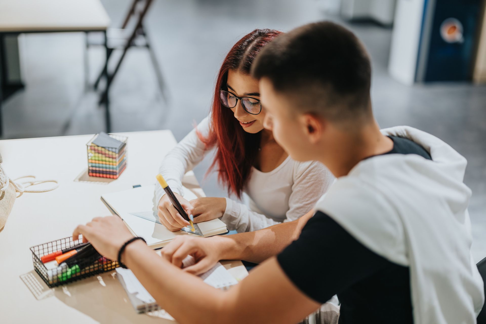 Two young people work together at a table, drawing with colorful markers.