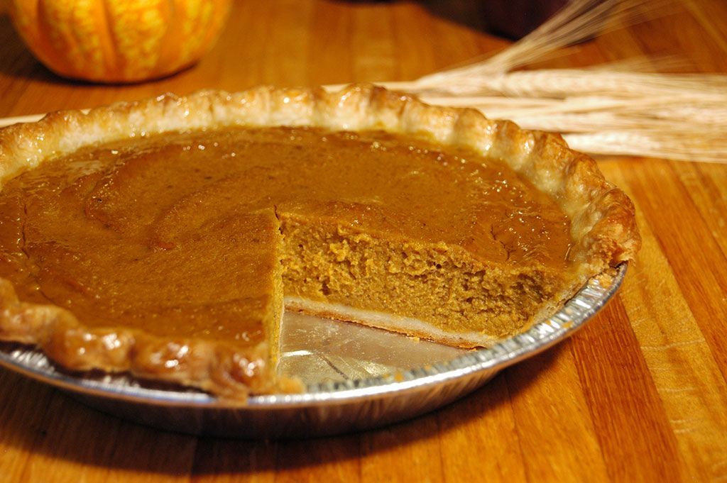 A pumpkin pie with a slice taken out of it is on a wooden table.
