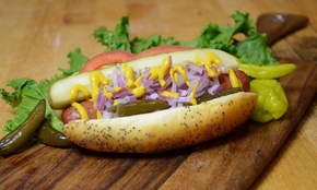 A hot dog with onions , mustard , pickles and lettuce on a wooden cutting board.