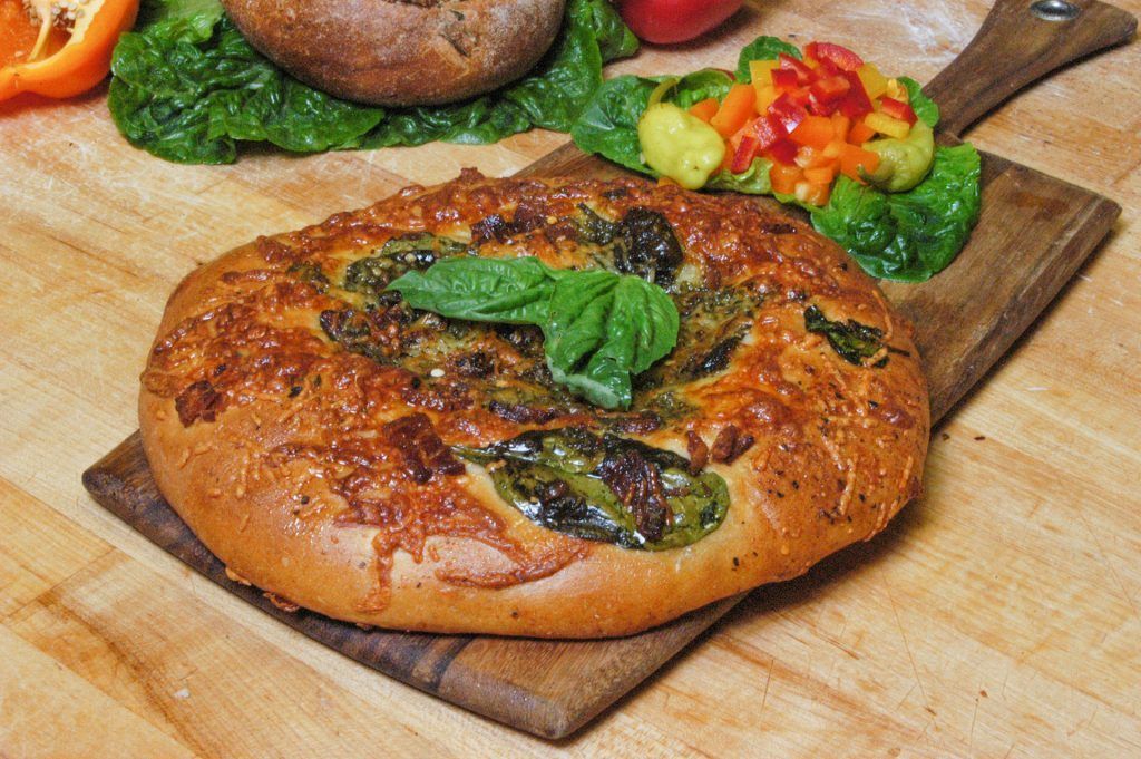 A pizza with spinach and cheese is sitting on a wooden cutting board.