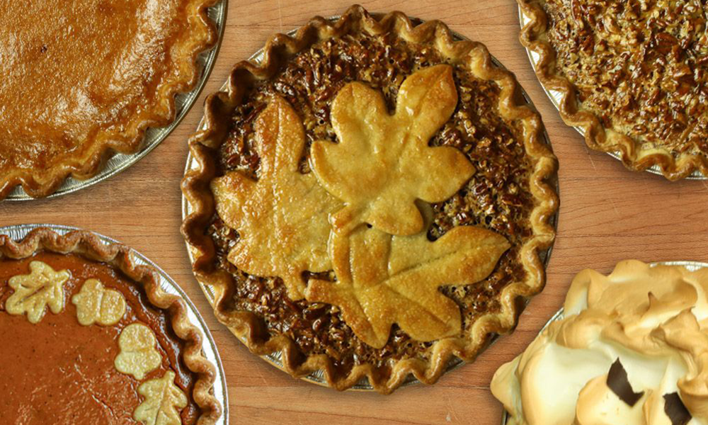 A variety of pies are sitting on a wooden table.