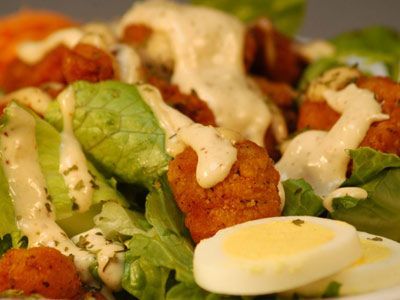 A close up of a salad with lettuce , chicken , eggs and dressing on a plate.
