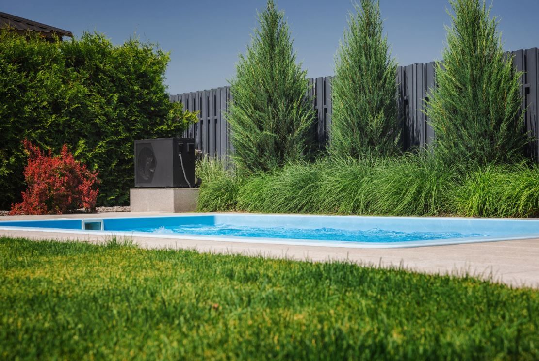 A modern pool heat pump heater installed in a backyard next to a swimming pool.