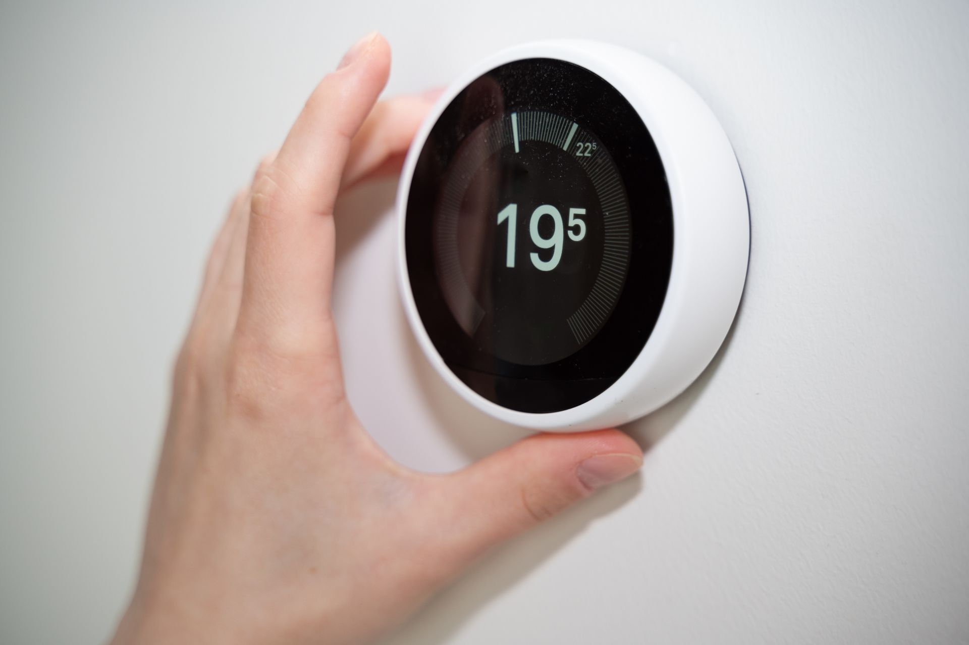 Hand adjusting a round, white thermostat displaying