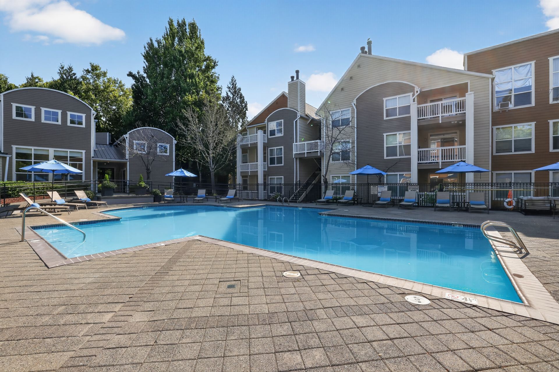Outdoor community pool with lounge chairs and green umbrellas.