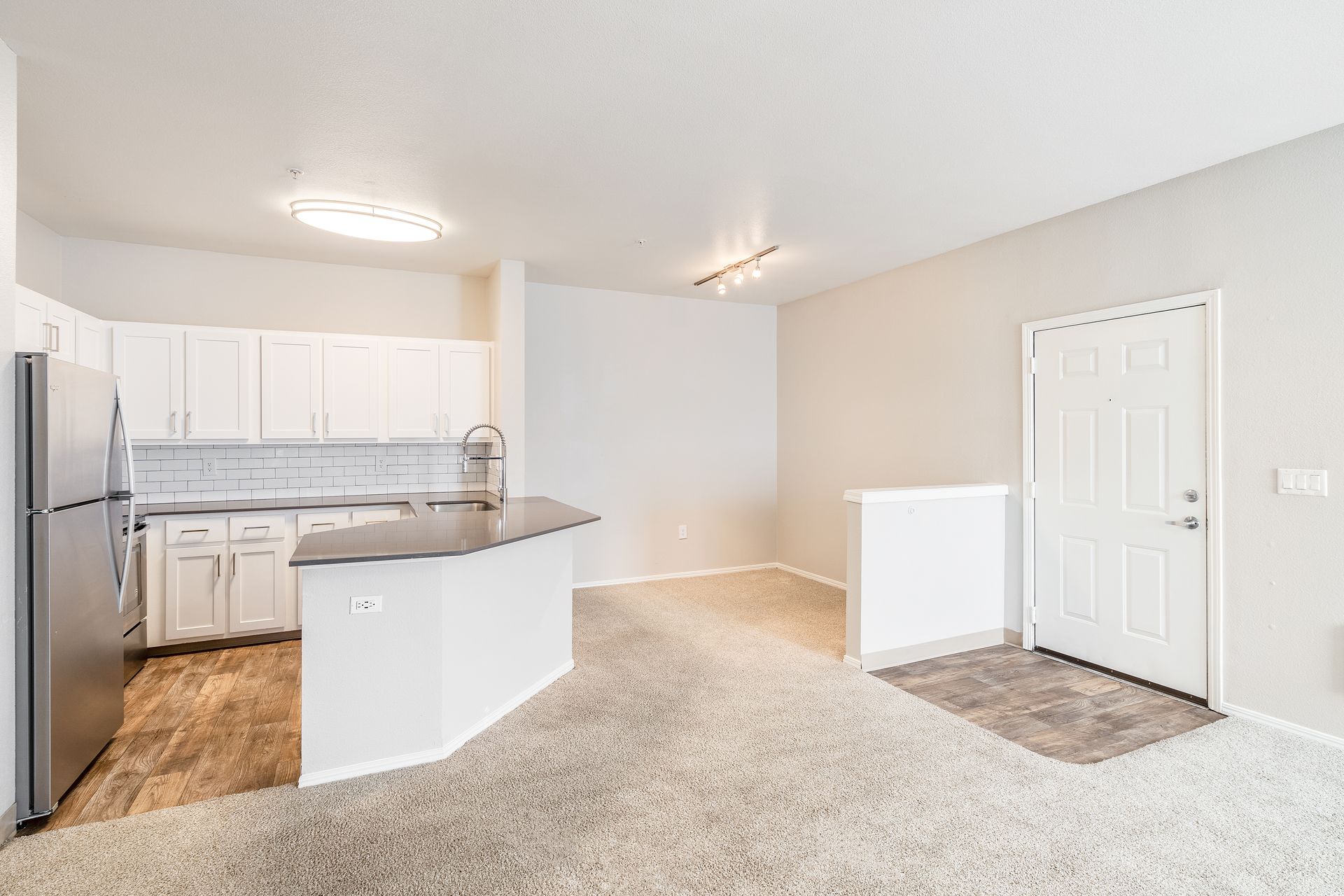 Bright open kitchen and living area with white cabinets, stainless fridge, and carpet in the living room
