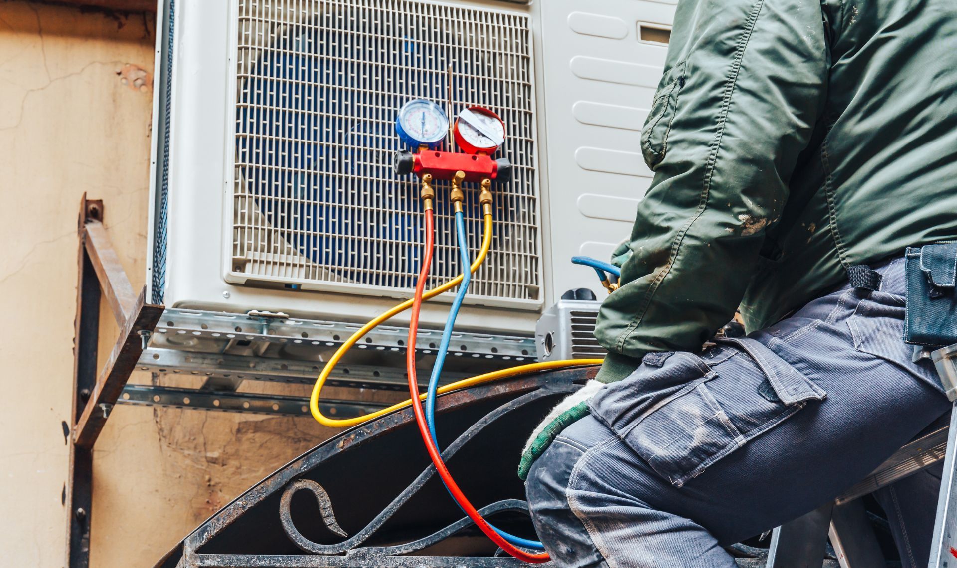 A man is sitting on a ladder working on an air conditioner.