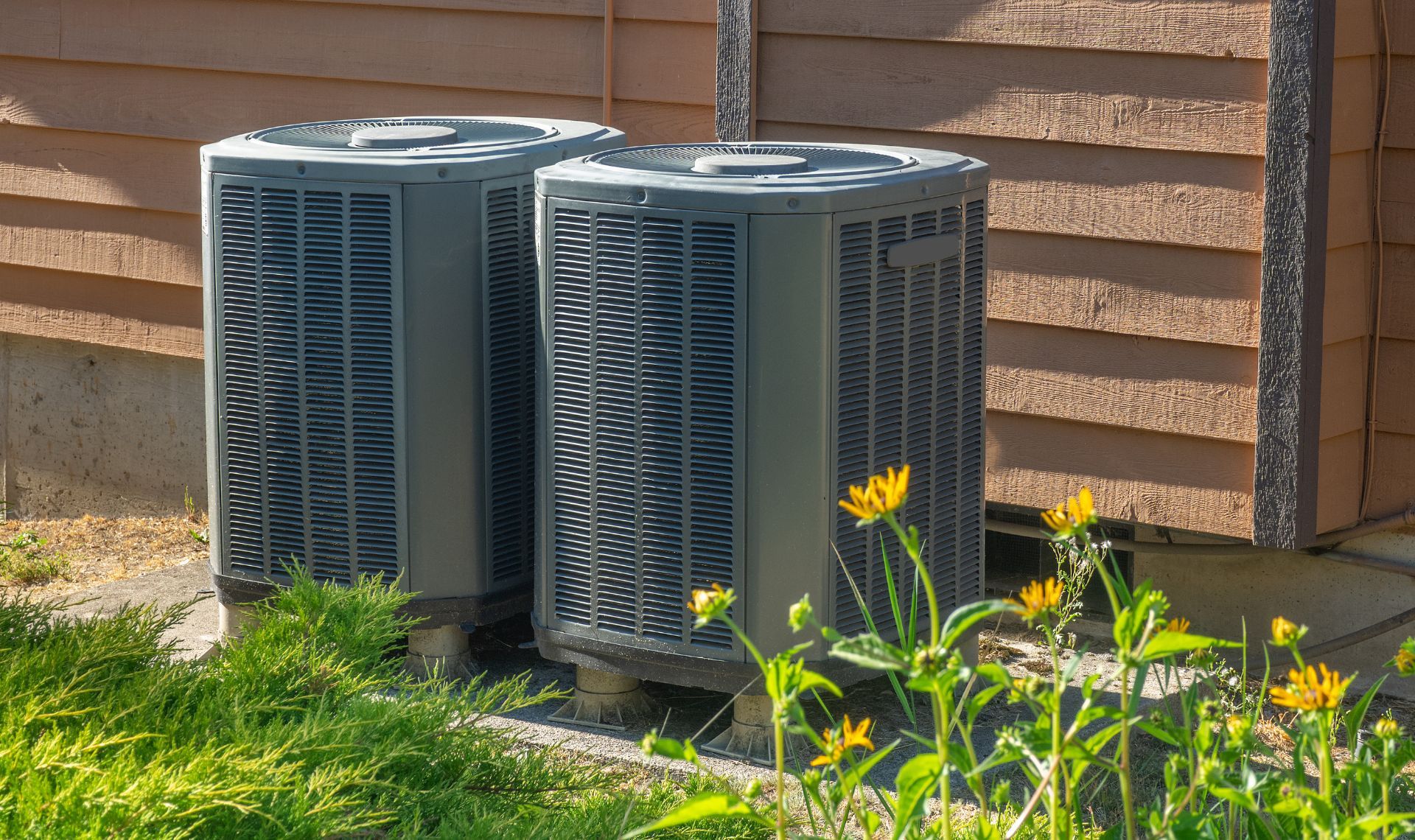Two air conditioners are sitting next to each other in front of a house.