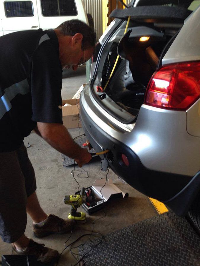 A Man is Working on the Back of a Silver Car — Cairns Auto Electrical Mechanical Air & Audio in Innisfail, QLD