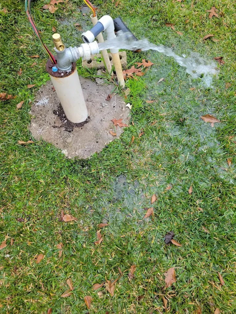 Leaking outdoor water pipe spraying onto grass beside a concrete post