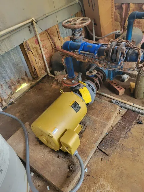 Industrial pump and piping system with a yellow motor in a worn utility room