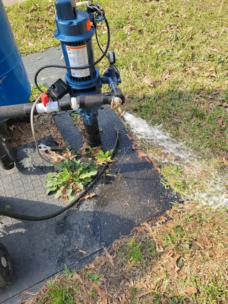 Blue water pump spraying water across a grassy sidewalk area