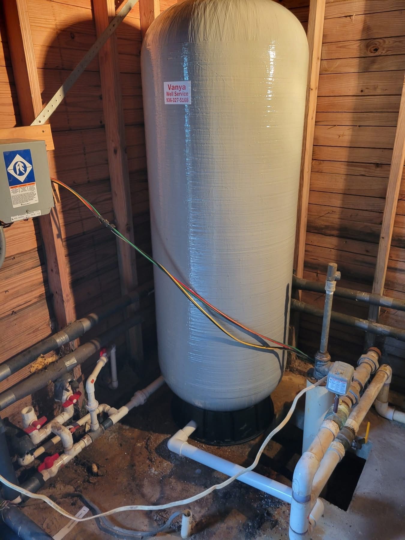 Large white pressure tank with pipes and valves in a wooden utility room