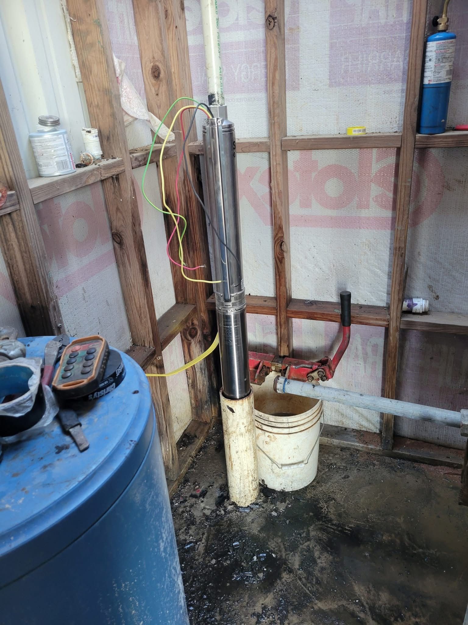 Basement utility area with blue tank, exposed pipes, and a white bucket on the floor.