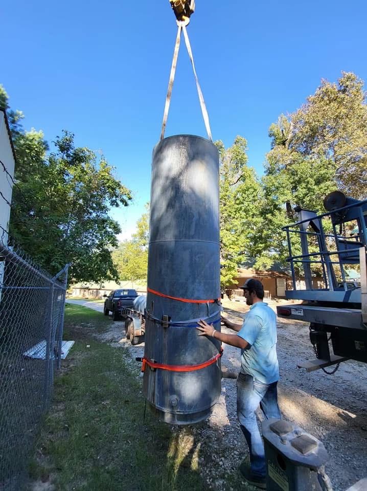 A large black cylindrical tank is being lifted by crane while a person guides it outdoors.