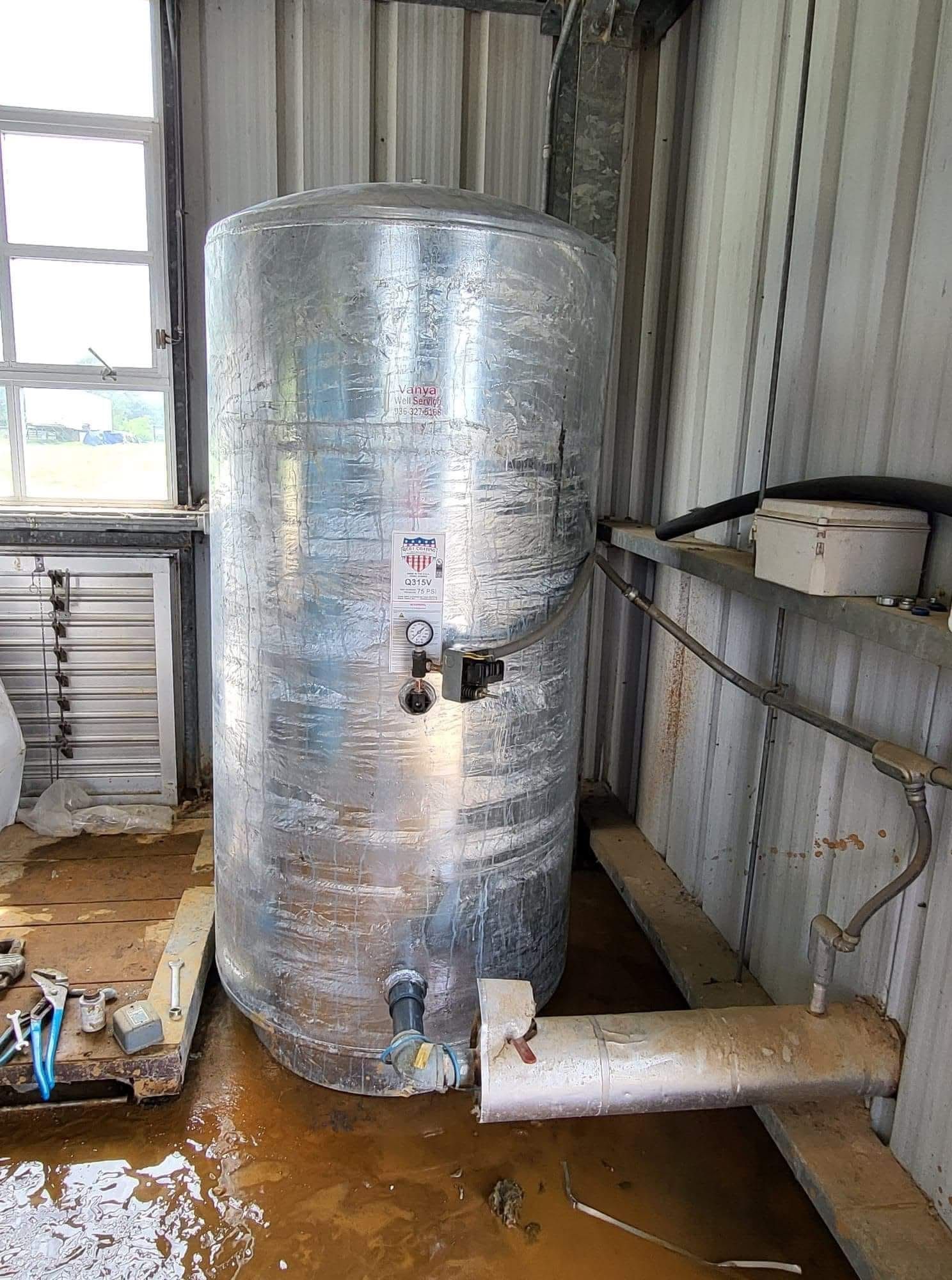 Large insulated metal tank with attached pipes inside a corrugated metal utility room