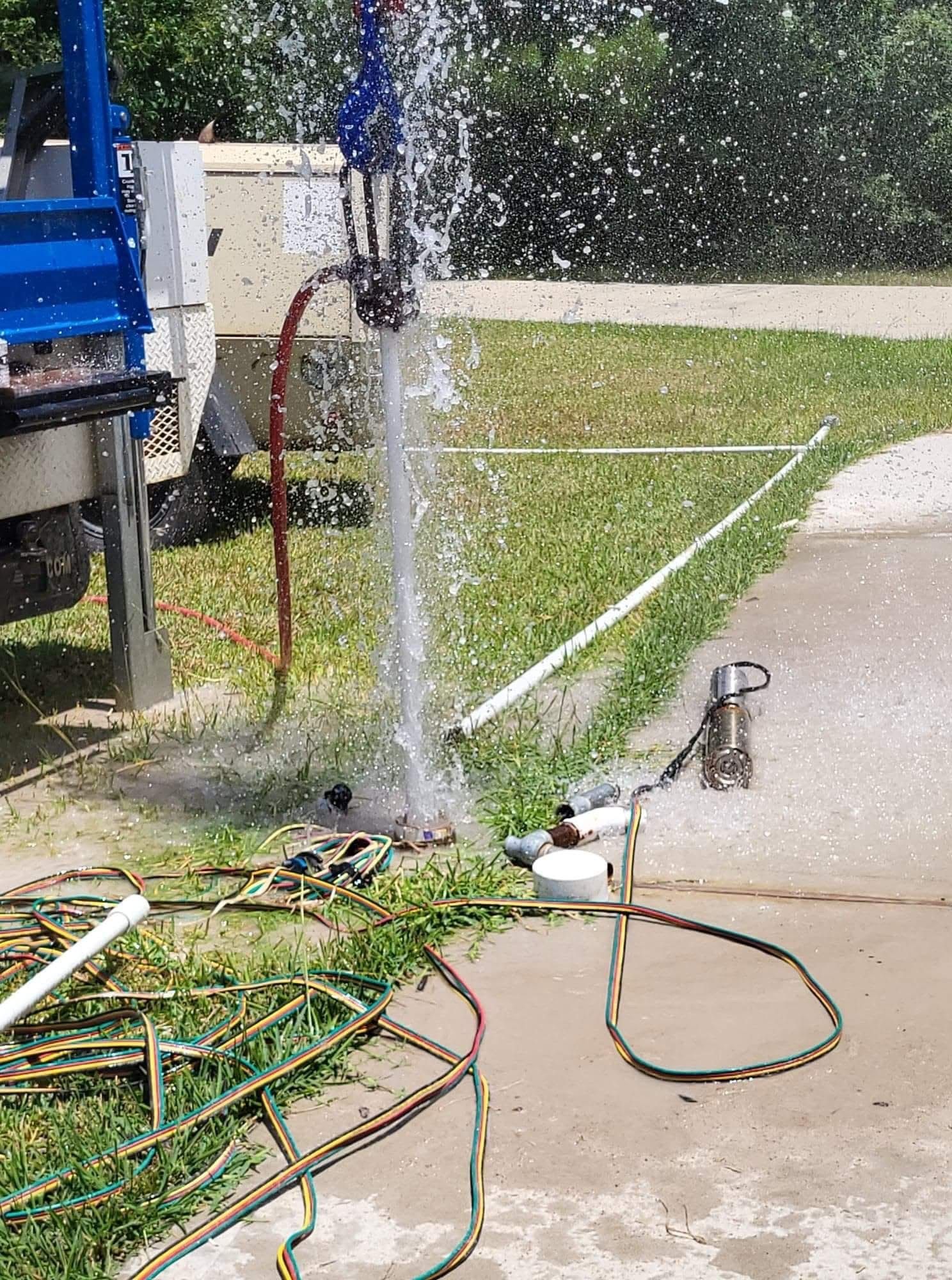 Broken water hose spraying water onto a driveway next to garden tools and a truck.