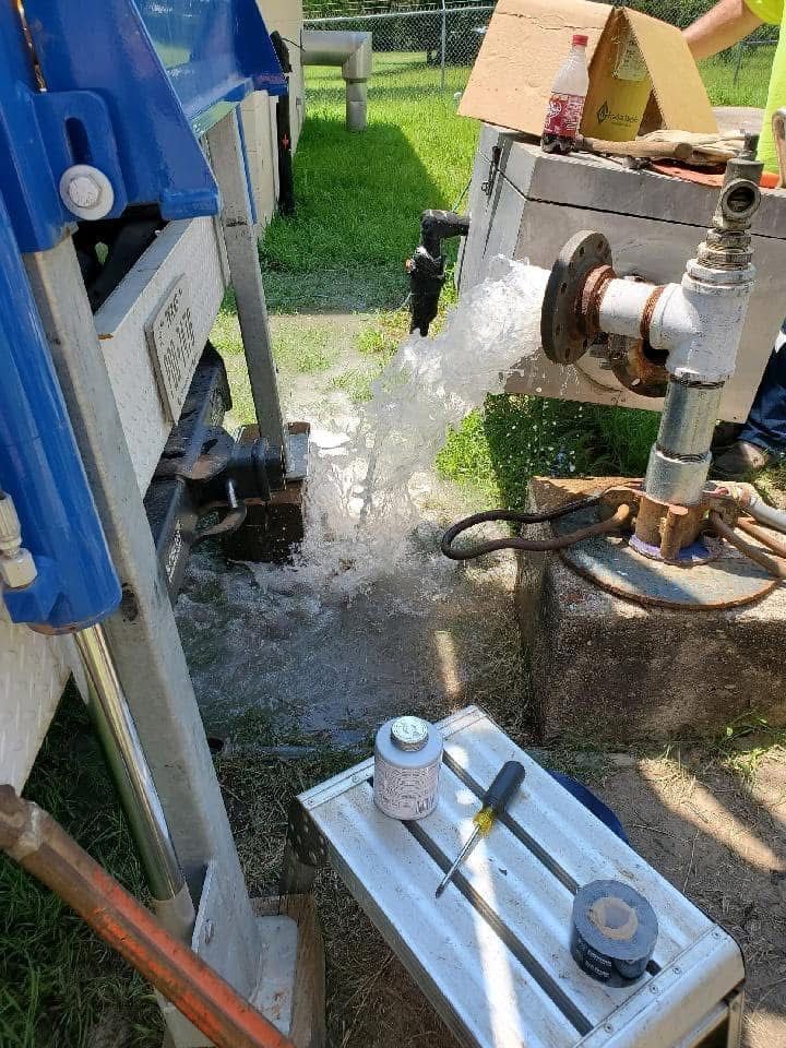 Blue machinery and white pipes spraying water into a grassy outdoor work area
