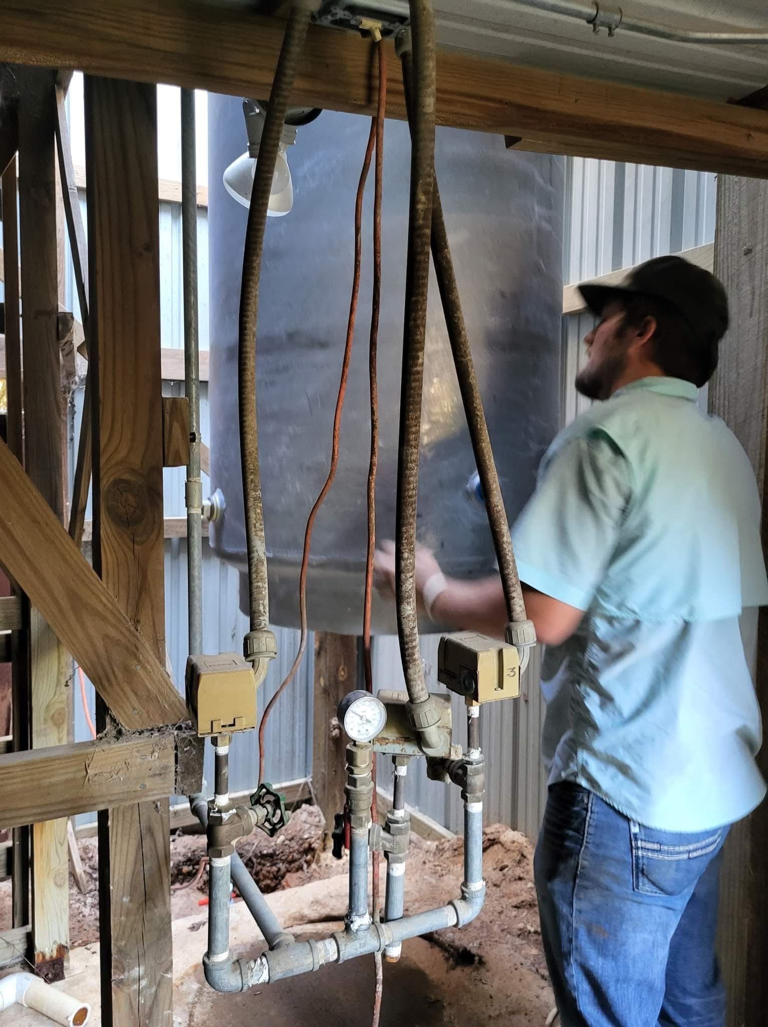 Worker in a light blue shirt inspecting plumbing in a wooden-framed construction site.