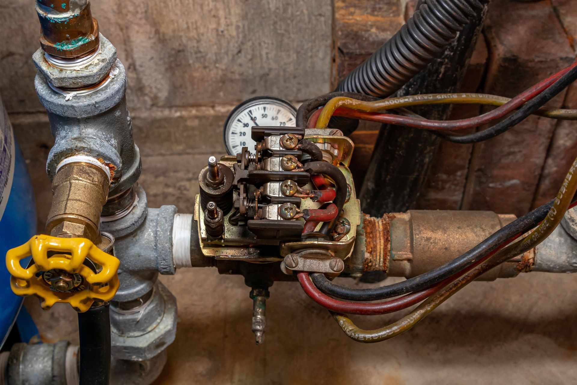 Close-up of a gas valve and electrical relay mounted on metal pipes, with wires attached