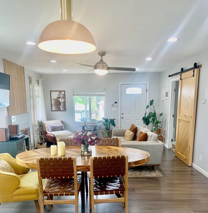Bright open living-dining room with yellow sofa, woven chairs, round table, ceiling fan, and sliding barn door