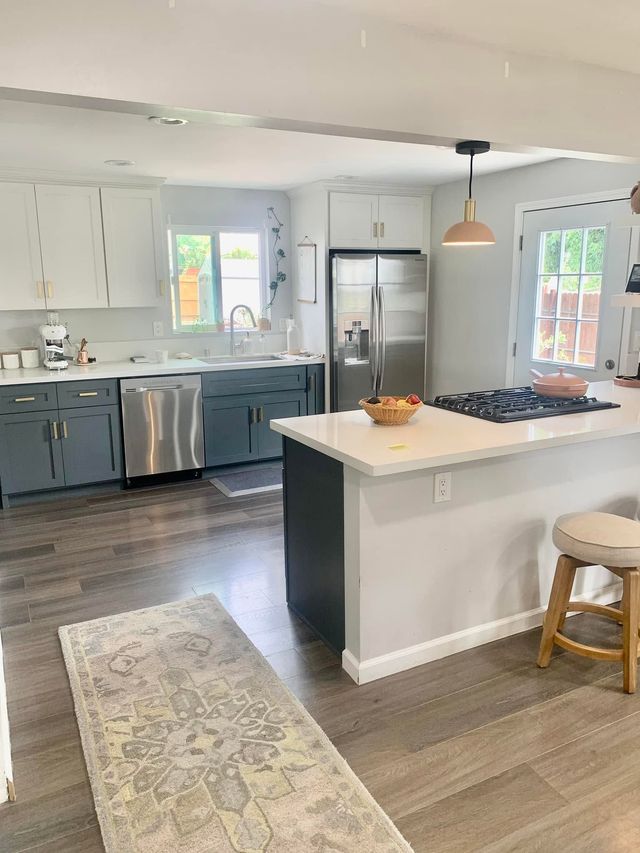 Bright modern kitchen with white island, blue cabinets, stainless appliances, and wood floors