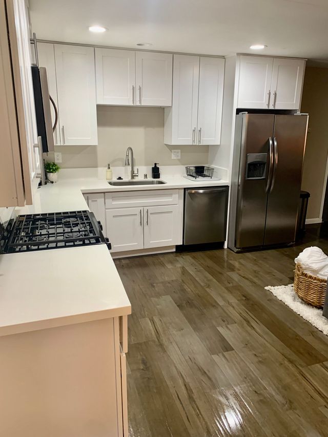 Bright modern kitchen with white cabinets, stainless steel appliances, and wood floors