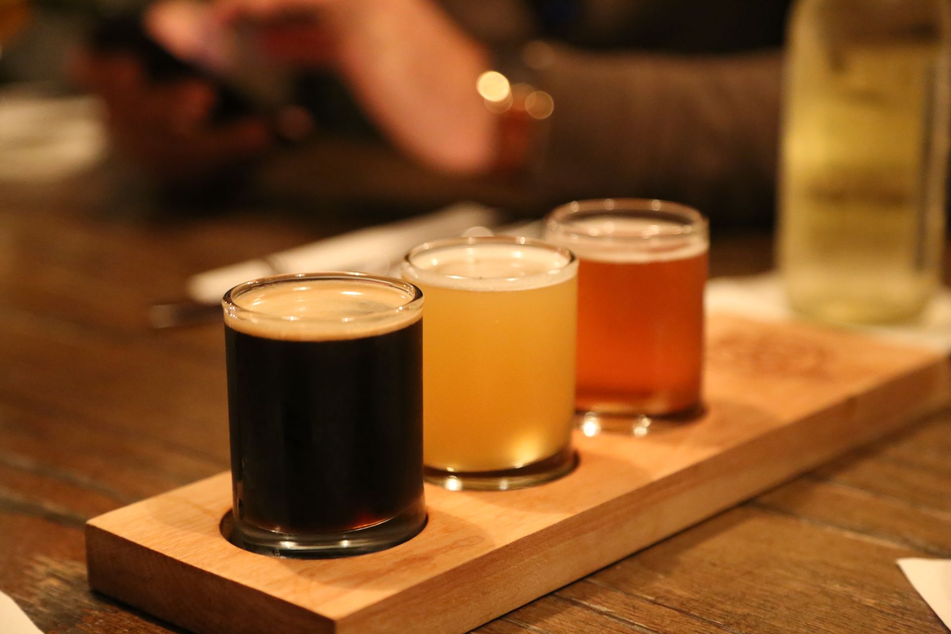 Three craft beer samples in glasses on a wooden tray at a bar