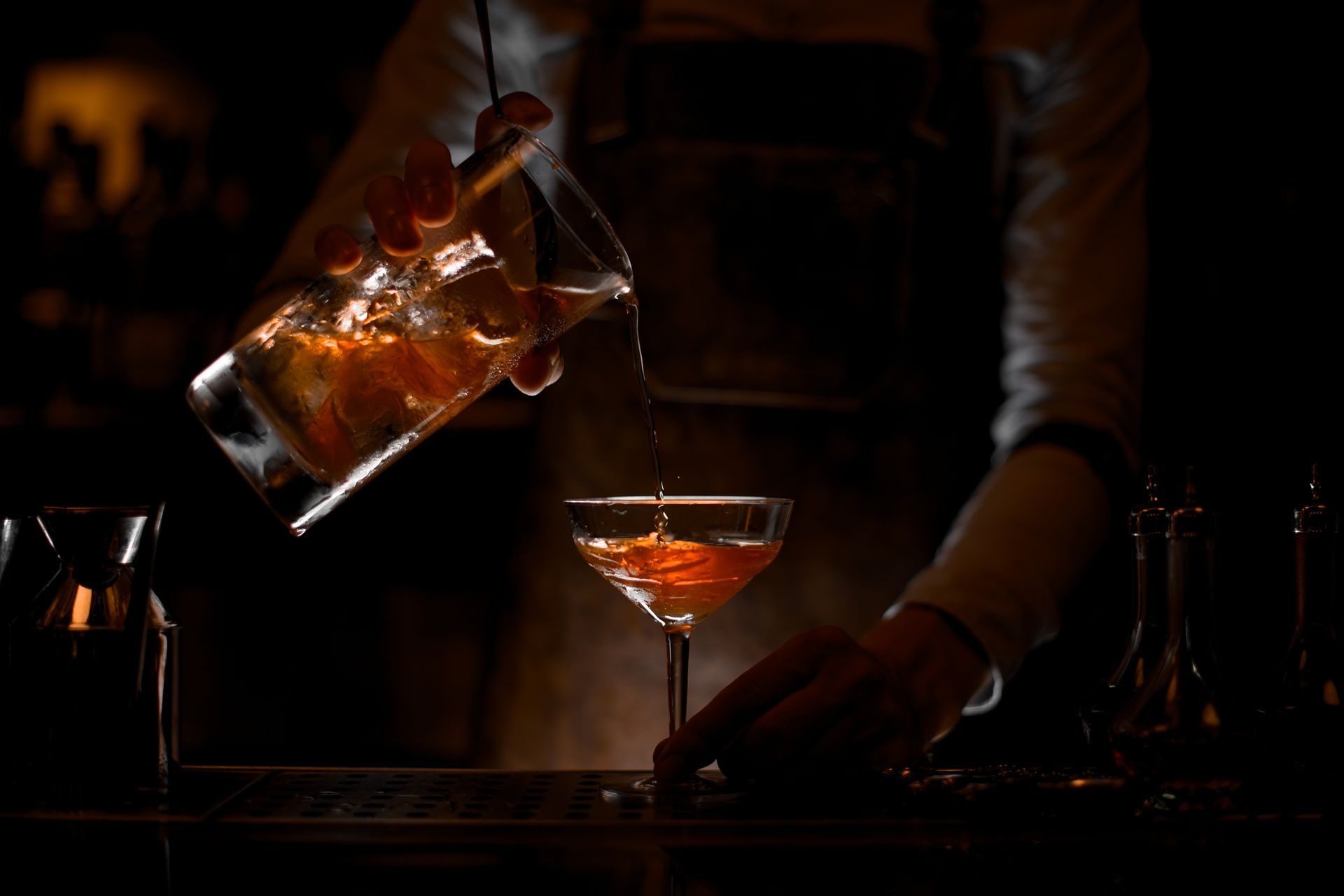 Bartender pouring amber liquor into a cocktail glass in a dimly lit bar