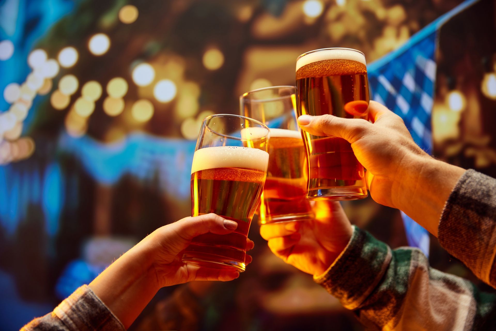 Friends toasting beer mugs at a lively outdoor party with colorful lights in the background