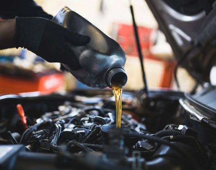 Gloved hand pouring motor oil into a car engine bay during maintenance