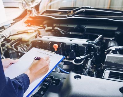 Mechanic inspecting a car engine while writing notes on a clipboard in a garage