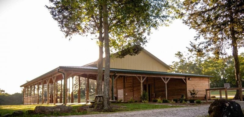 Rustic wooden lodge with a wraparound porch among tall trees in warm sunlight