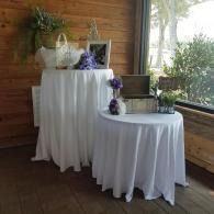 Two draped tables with purple floral arrangements in a rustic indoor setting