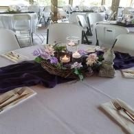 Decorated banquet table with purple runner, floral centerpiece, and candles in a bright event hall