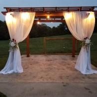 Decorated outdoor pergola with white drapes and warm string lights at dusk