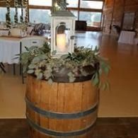 Wooden barrel planter with white flowers and a lantern in a warmly lit indoor space